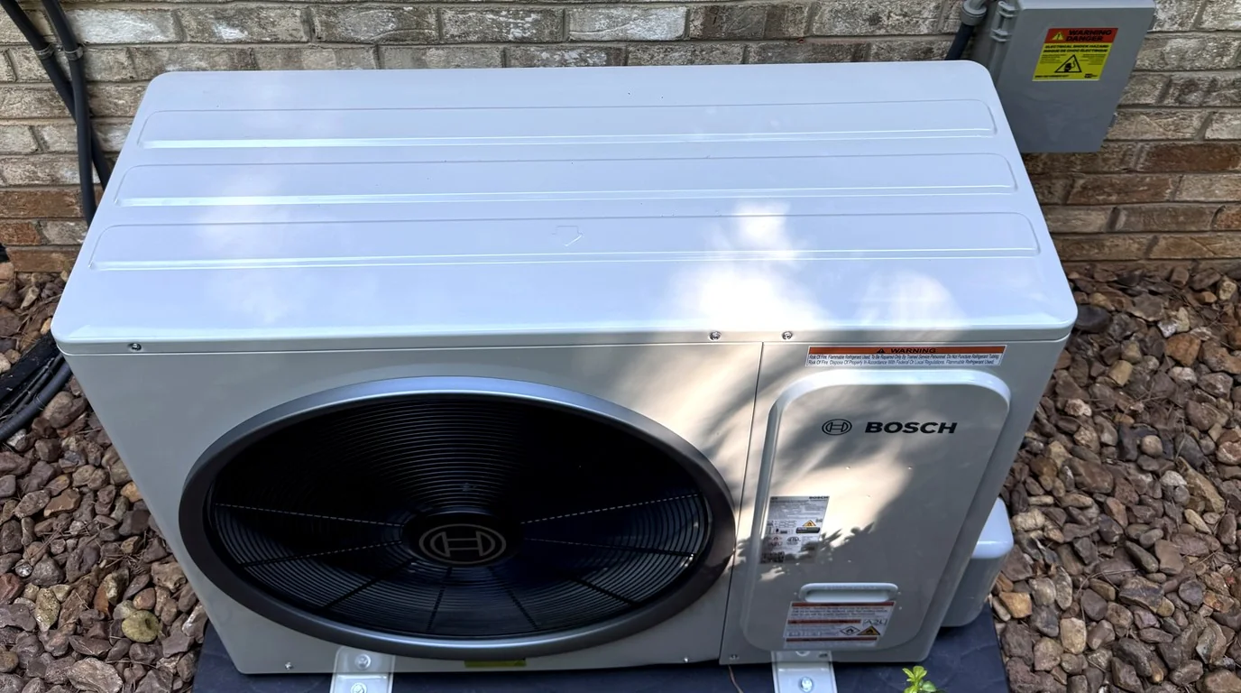 Outdoor heat pump unit on a pad against brick, the kind of system heat pump repair calls in Belmont NC involve